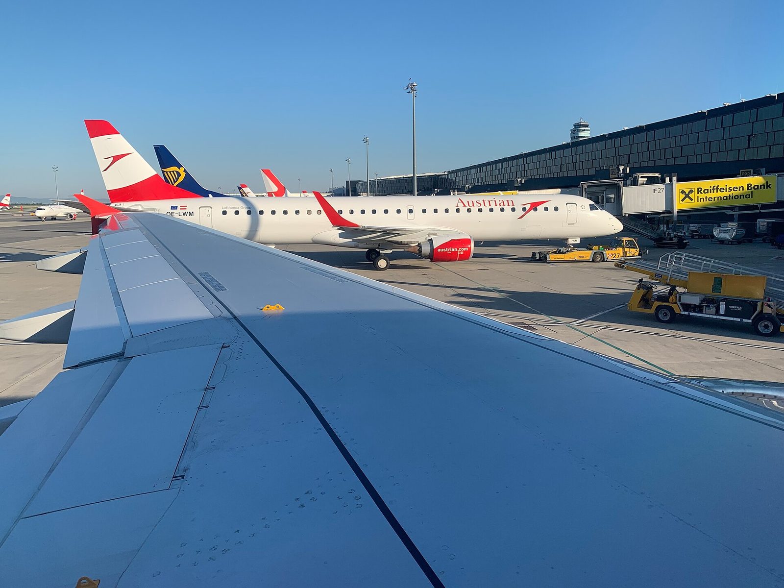 Austrian-Airlines-Flugzeug am Gate des Flughafens Wien-Schwechat (VIE) mit Tower und Terminal im Hintergrund.